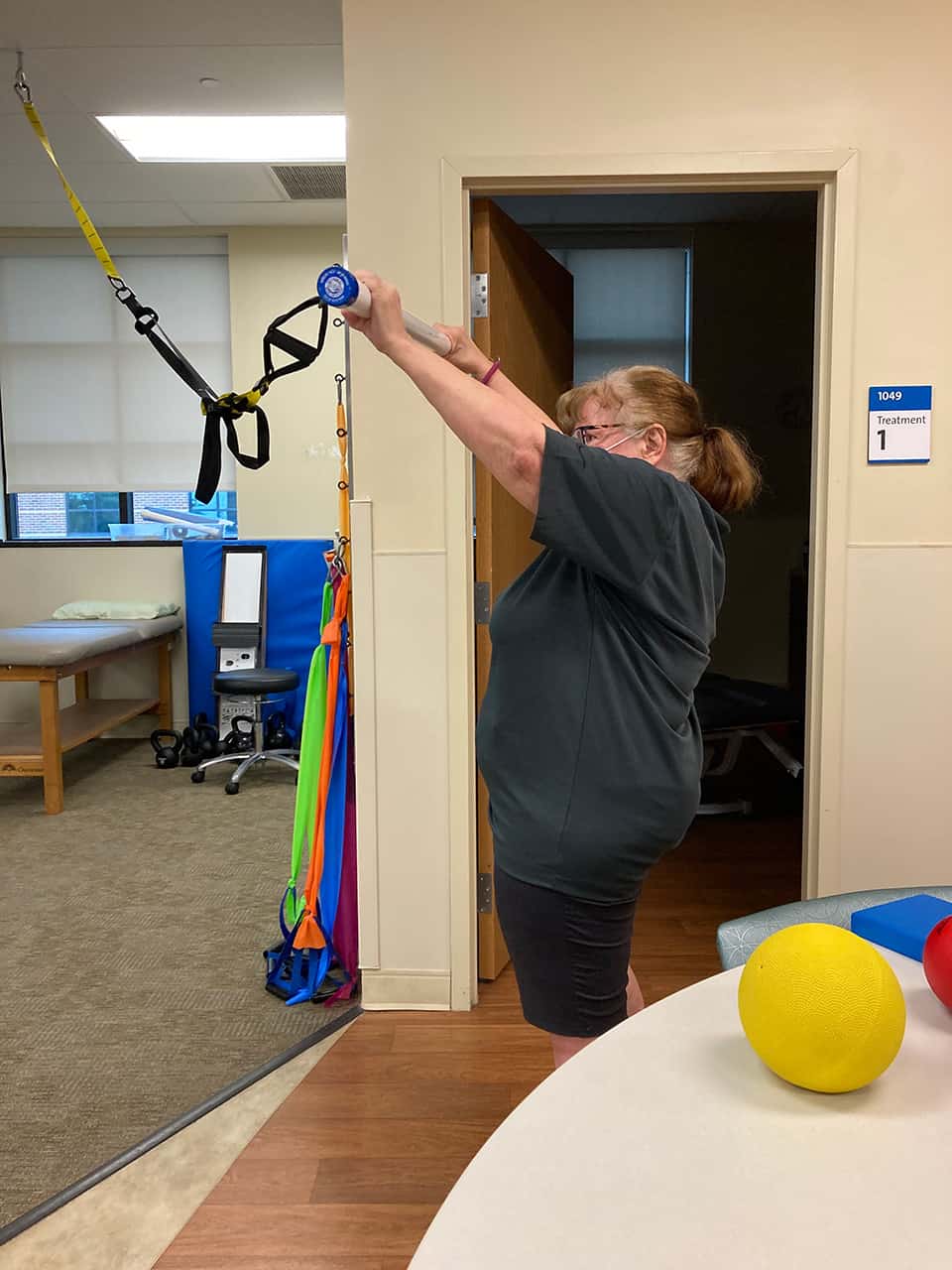 Susan Foley performing shoulder exercises in a treatment room.